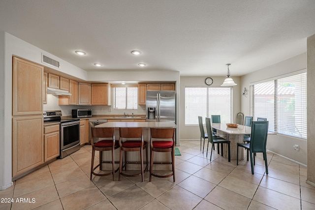 kitchen with appliances with stainless steel finishes, a kitchen island, pendant lighting, and light tile patterned floors