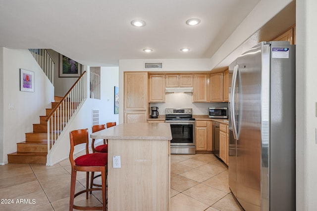 kitchen with a center island, light tile patterned flooring, appliances with stainless steel finishes, light brown cabinetry, and a kitchen breakfast bar