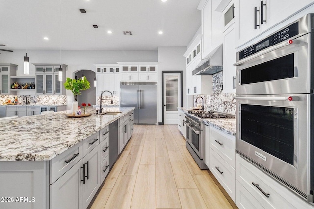 kitchen featuring sink, wall chimney exhaust hood, decorative backsplash, white cabinets, and high end appliances