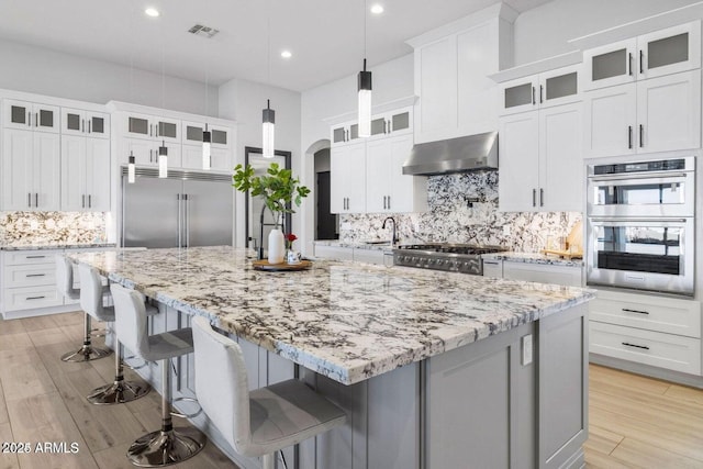 kitchen with a spacious island, range hood, a kitchen bar, white cabinetry, and stainless steel appliances