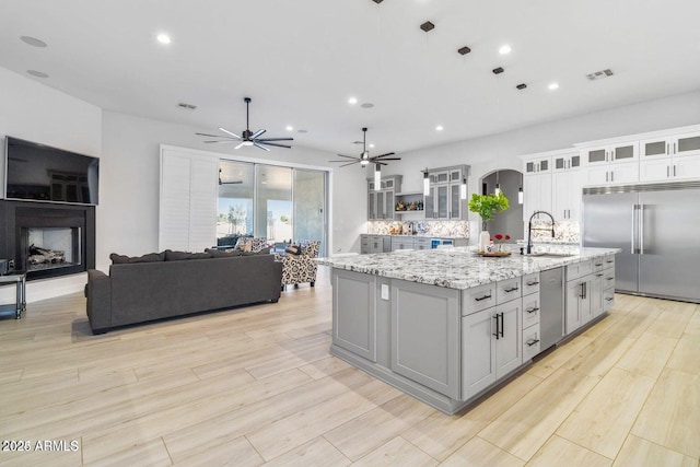 kitchen with light stone countertops, sink, built in fridge, backsplash, and a center island with sink