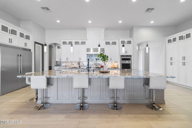 kitchen featuring a large island with sink, stainless steel appliances, and light stone counters