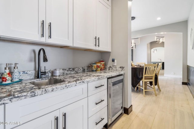 kitchen with light stone countertops, white cabinetry, sink, and wine cooler