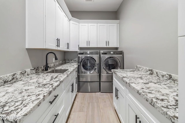 clothes washing area with washer and dryer, sink, cabinets, and light hardwood / wood-style flooring