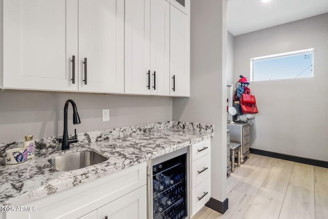 kitchen featuring light stone countertops, white cabinetry, beverage cooler, and sink