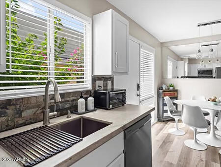 kitchen featuring sink, decorative light fixtures, light wood-type flooring, dishwasher, and white cabinets