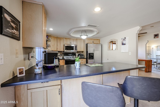 kitchen with light tile patterned floors, stainless steel appliances, light brown cabinets, and decorative light fixtures