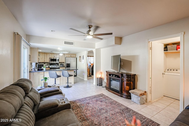 living room featuring ceiling fan, light tile patterned floors, and washer / dryer