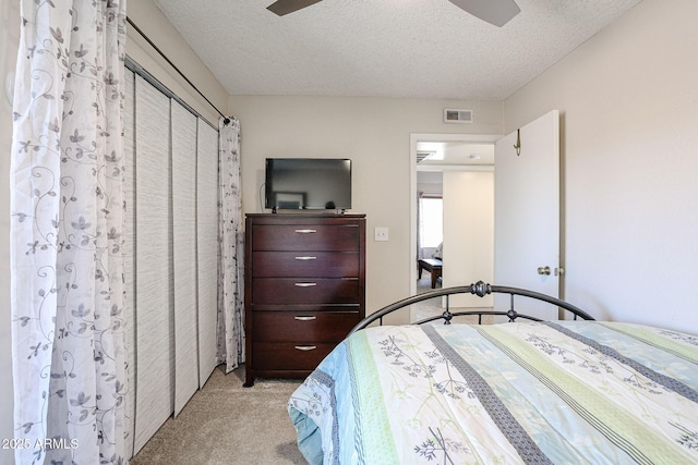 bedroom with ceiling fan, light colored carpet, a textured ceiling, and a closet