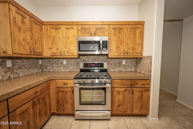 40808 N Raleigh Ct, Anthem, AZ 85086 - kitchen featuring stainless steel appliances, light tile patterned flooring, brown cabinets, tasteful backsplash, and baseboards