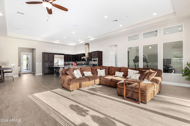 living room with ceiling fan, light wood-type flooring, and a tray ceiling