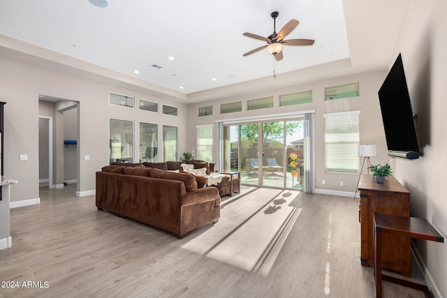 living room with light wood-type flooring, a tray ceiling, and ceiling fan