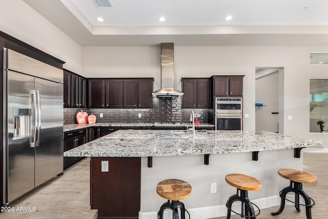 kitchen featuring a large island with sink, a breakfast bar area, stainless steel appliances, and wall chimney range hood