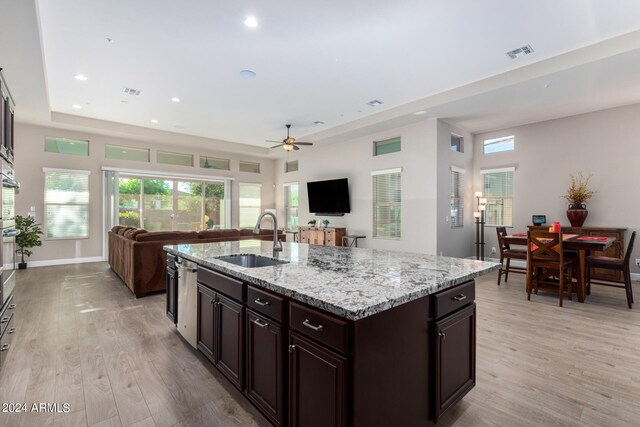 kitchen with light stone countertops, a center island with sink, sink, ceiling fan, and light wood-type flooring