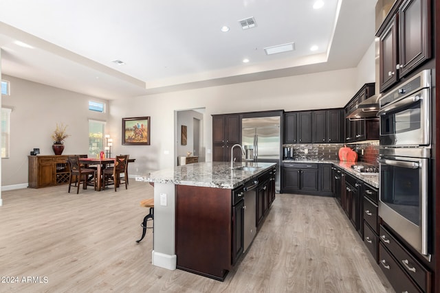 kitchen with a kitchen breakfast bar, light stone countertops, a center island with sink, light hardwood / wood-style flooring, and stainless steel appliances