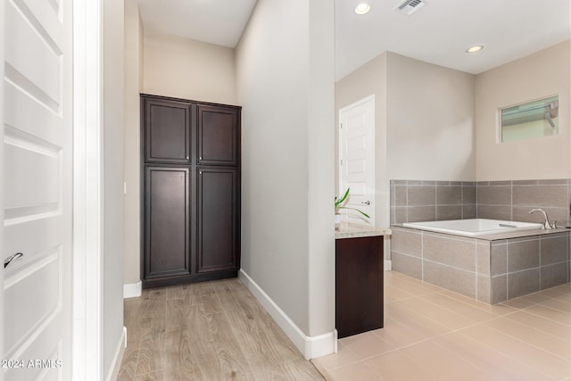 bathroom featuring hardwood / wood-style floors, tiled tub, and vanity