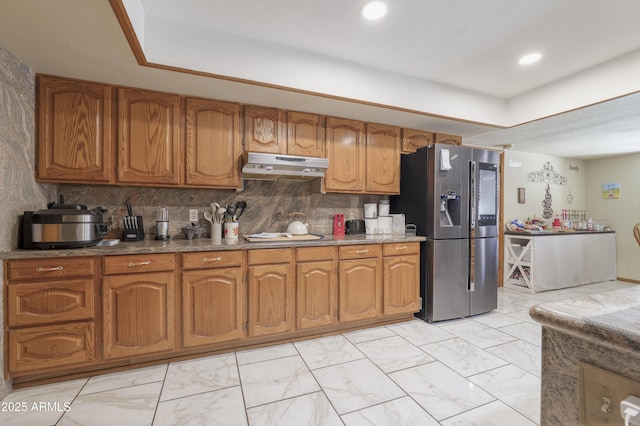 1285 E Mcmurray Blvd, Casa Grande, AZ 85122 - kitchen with stainless steel fridge with ice dispenser, under cabinet range hood, brown cabinetry, light marble finish flooring, and backsplash
