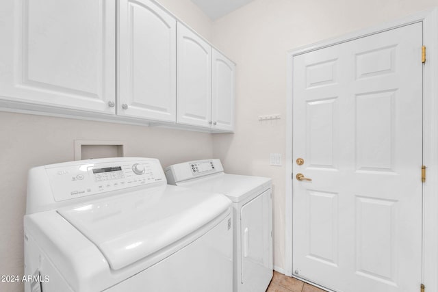 clothes washing area with separate washer and dryer, cabinets, and light tile patterned floors