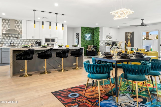 interior space featuring wall chimney range hood, decorative backsplash, light hardwood / wood-style flooring, a breakfast bar, and white cabinetry