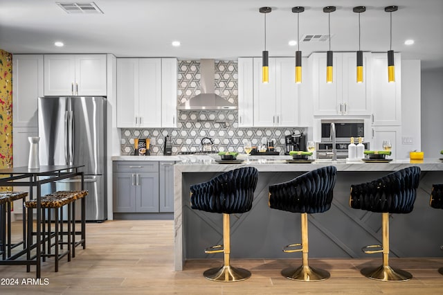 kitchen featuring wall chimney exhaust hood, white cabinets, backsplash, and stainless steel appliances