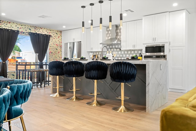 kitchen featuring light wood-type flooring, a breakfast bar area, stainless steel appliances, and wall chimney exhaust hood