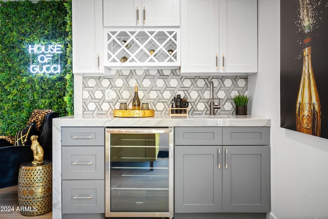 bar with backsplash, beverage cooler, gray cabinets, and light stone countertops