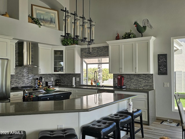 kitchen featuring wall chimney exhaust hood, white cabinetry, a breakfast bar area, and appliances with stainless steel finishes