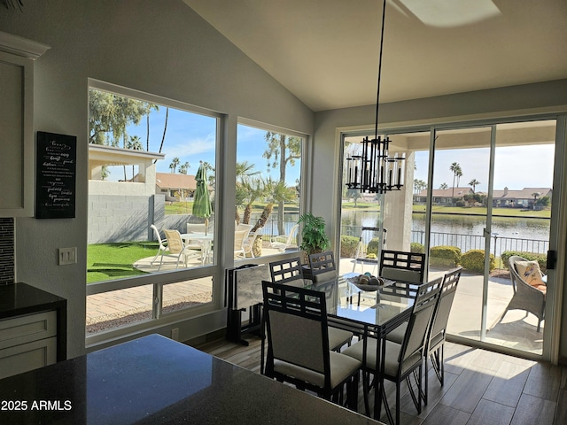 dining space with hardwood / wood-style floors, a water view, a chandelier, and lofted ceiling