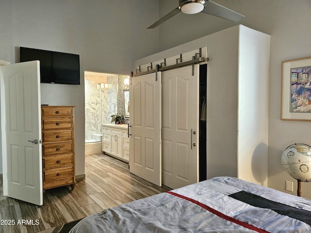 bedroom with light hardwood / wood-style flooring, ceiling fan, a barn door, connected bathroom, and a closet