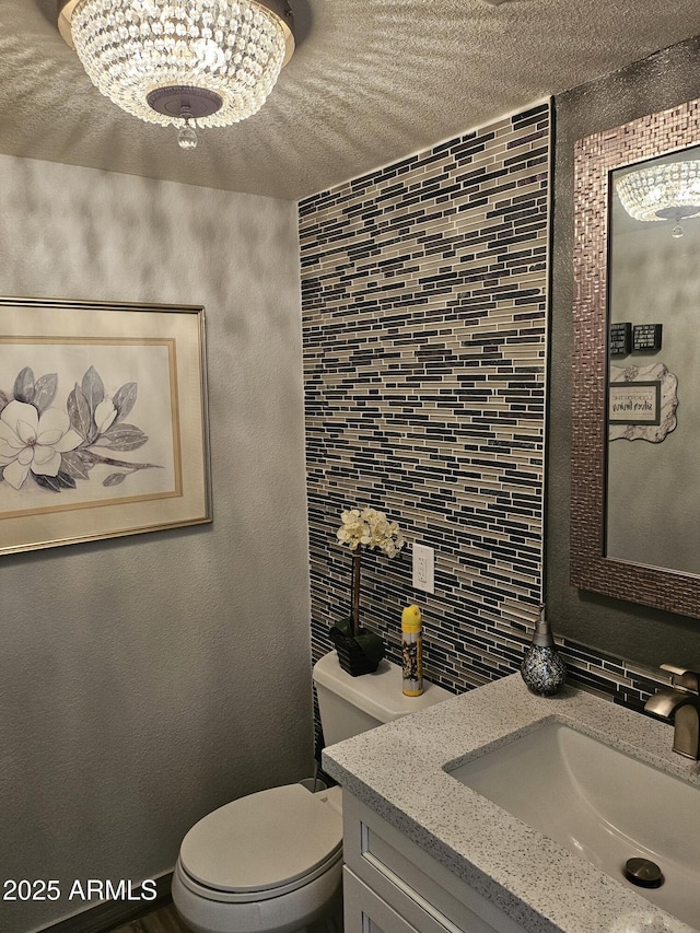 bathroom featuring decorative backsplash, a textured ceiling, vanity, a chandelier, and toilet