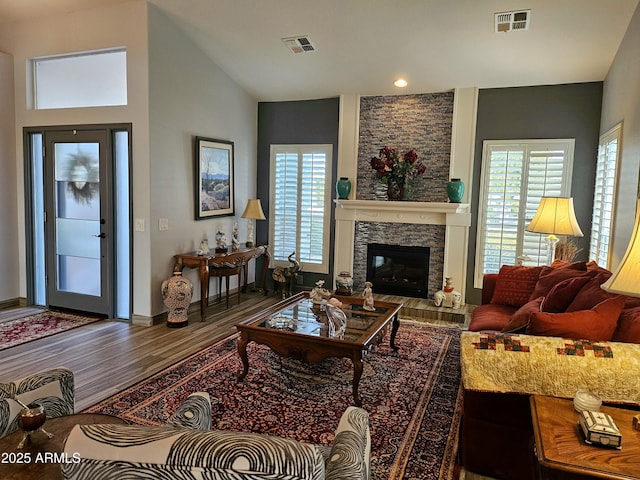 living room with vaulted ceiling, hardwood / wood-style flooring, a stone fireplace, and plenty of natural light