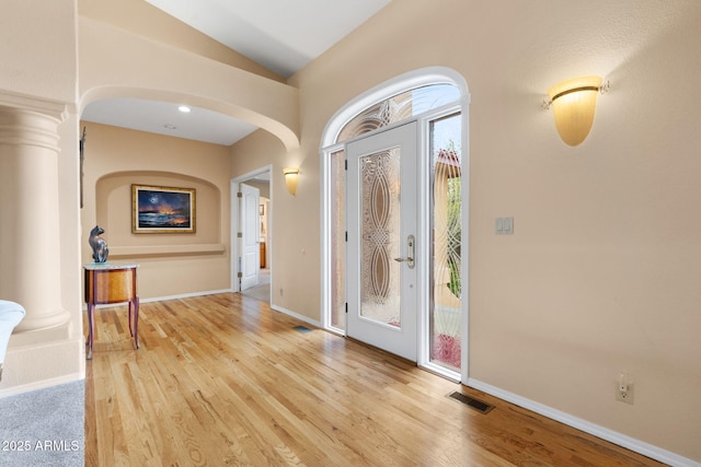 foyer entrance with visible vents, lofted ceiling, decorative columns, light wood-style flooring, and arched walkways