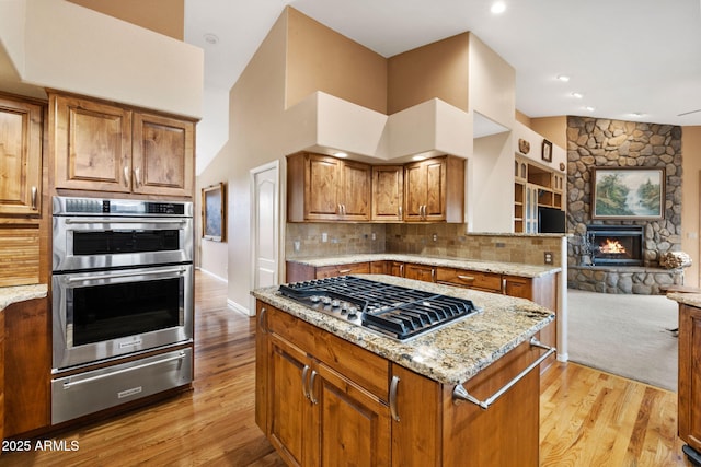 kitchen featuring a warming drawer, light stone counters, open floor plan, stainless steel appliances, and light wood finished floors