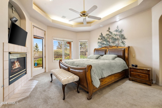 bedroom featuring access to exterior, a fireplace, light carpet, and a tray ceiling