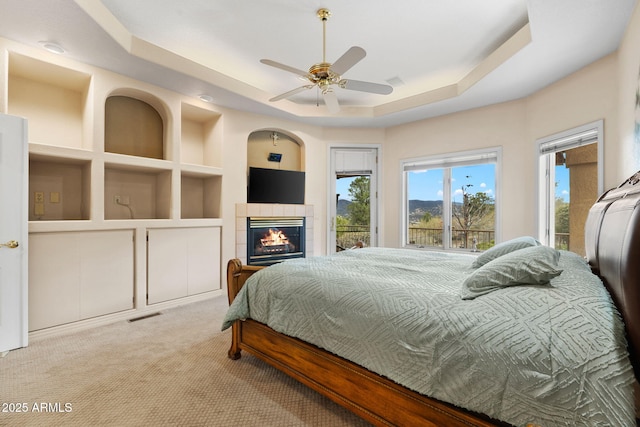 bedroom featuring visible vents, a tray ceiling, carpet floors, access to exterior, and a tile fireplace