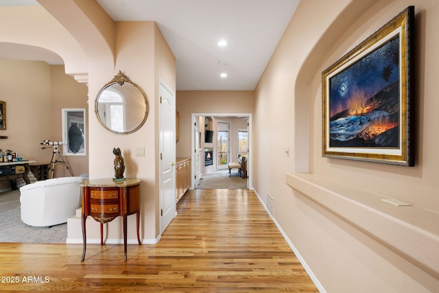 hall with arched walkways, visible vents, light wood-type flooring, and baseboards