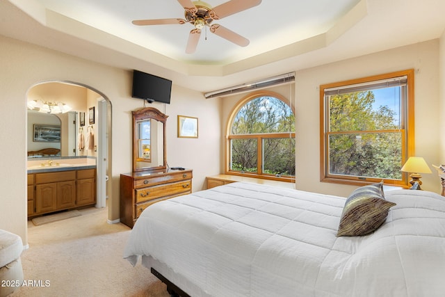 bedroom with a sink, ensuite bath, arched walkways, a raised ceiling, and light colored carpet