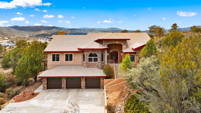 view of front facade featuring driveway, an attached garage, a chimney, stone siding, and a mountain view