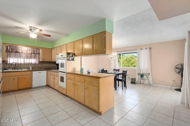 kitchen featuring ceiling fan with notable chandelier, white appliances, sink, kitchen peninsula, and light tile patterned floors