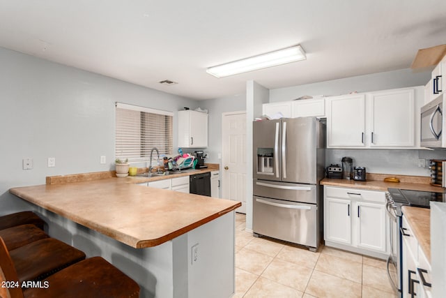 kitchen with appliances with stainless steel finishes, a breakfast bar area, sink, light tile patterned flooring, and kitchen peninsula