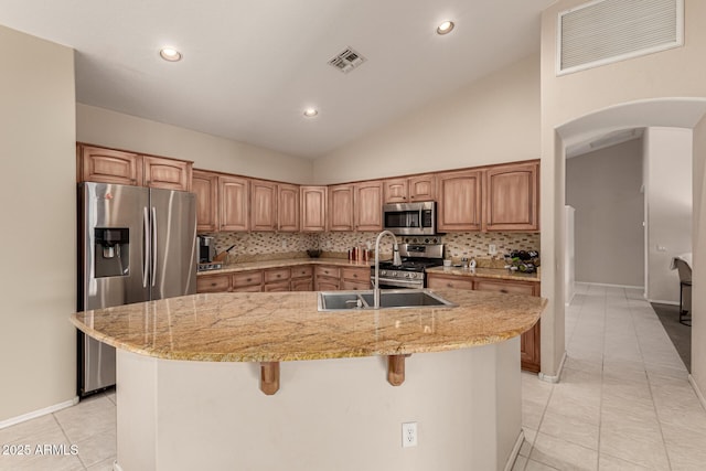 kitchen featuring appliances with stainless steel finishes, a kitchen island with sink, light tile patterned floors, and decorative backsplash