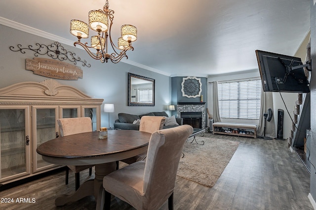 dining area with dark wood-type flooring, ornamental molding, an inviting chandelier, and a fireplace