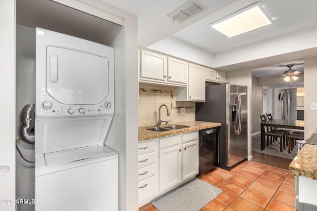 kitchen featuring black dishwasher, sink, white cabinets, decorative backsplash, and stacked washer and clothes dryer