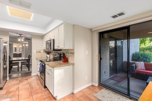 kitchen featuring appliances with stainless steel finishes, light stone countertops, white cabinets, light tile patterned flooring, and decorative backsplash