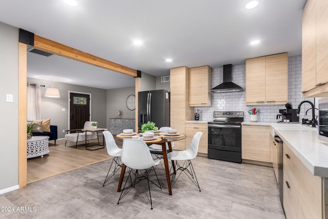 kitchen with light brown cabinetry, appliances with stainless steel finishes, wall chimney range hood, and light wood-type flooring