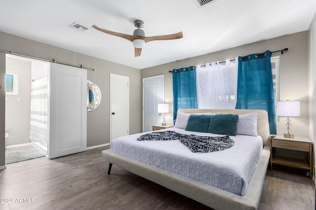 bedroom with hardwood / wood-style floors, a barn door, and ceiling fan