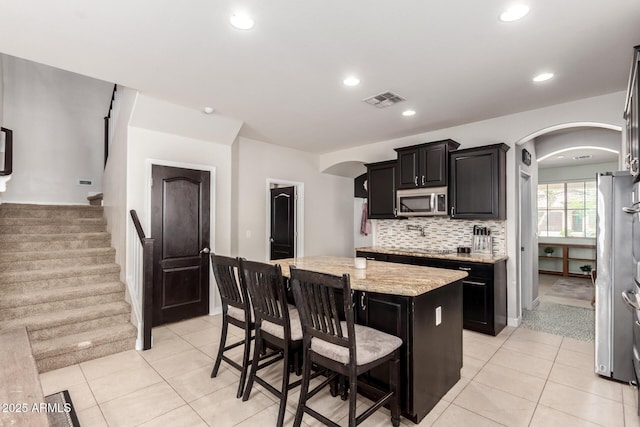 20709 W Delaney Dr, Buckeye, AZ 85396 - kitchen with arched walkways, a kitchen island, light tile patterned flooring, stainless steel microwave, and recessed lighting