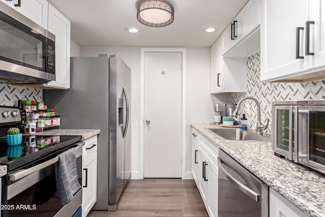 kitchen with white cabinets, appliances with stainless steel finishes, light stone countertops, light wood-style floors, and a sink