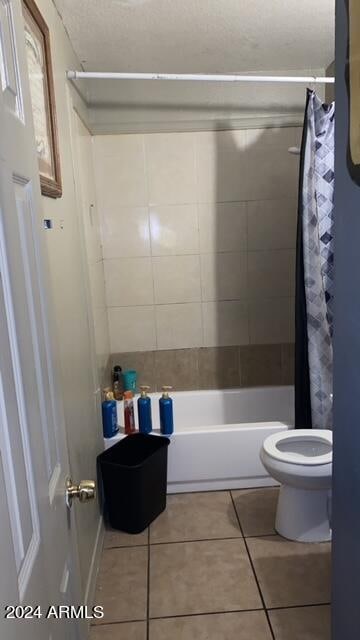 bathroom featuring shower / bathtub combination with curtain, tile patterned flooring, and toilet