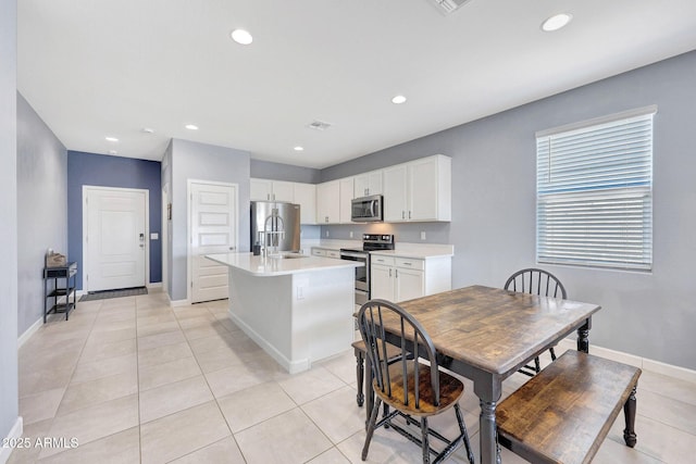 kitchen with a center island with sink, light countertops, white cabinetry, appliances with stainless steel finishes, and light tile patterned floors